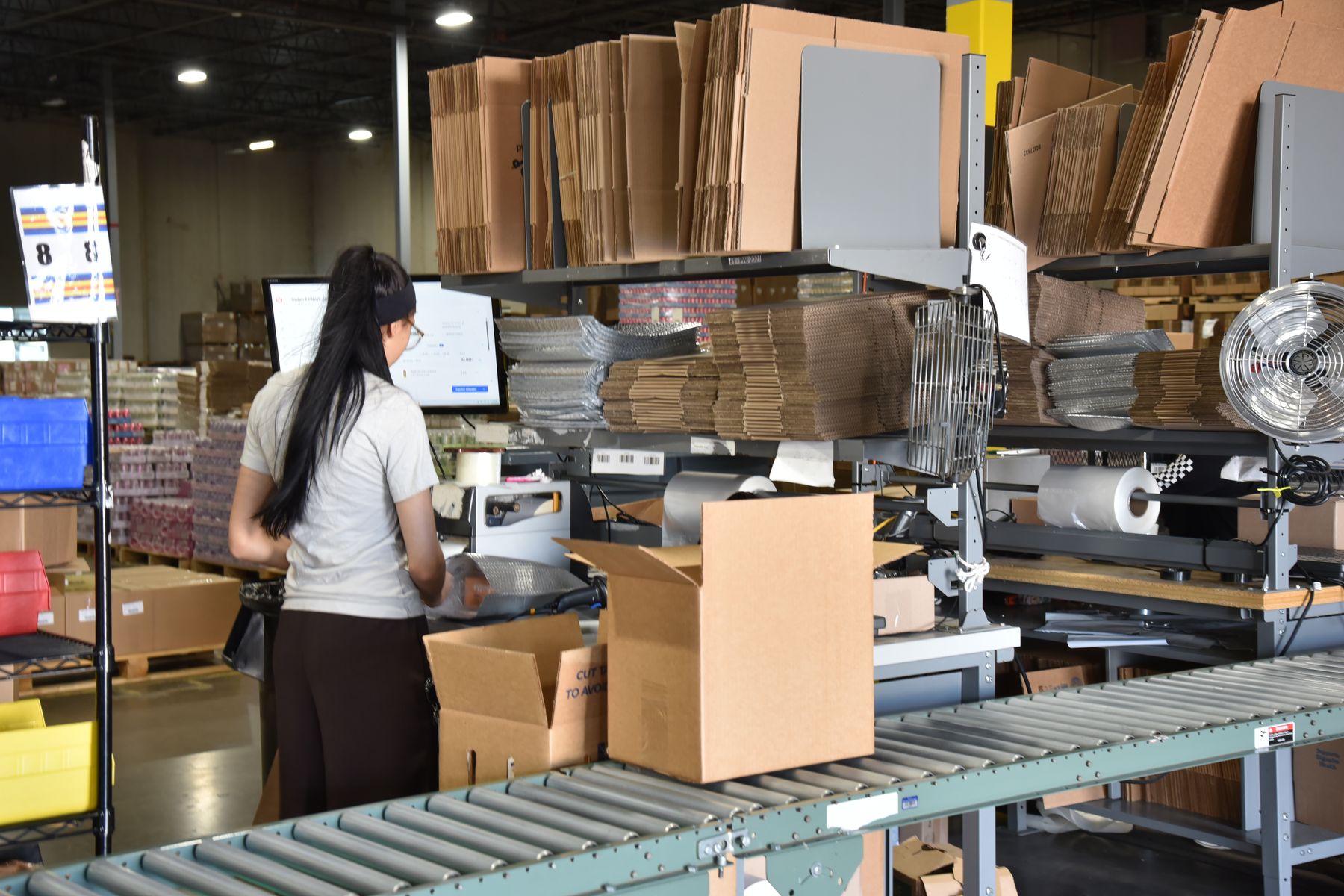 Team member at a pack station with an order screen, shipping supplies and a roller conveyor